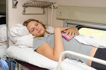 Image showing The girl in a train sleeping at the back on the top shelf and the side with the magazine in an embrace