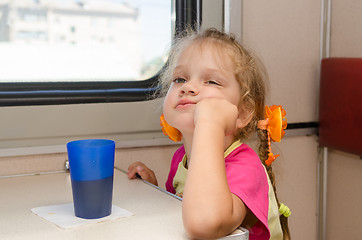 Image showing A girl of four years of thoughtful and tired of sitting on the train at the table on the side a place reserved seat