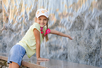 Image showing Girl in summer clothes with a smile stretching his hand to water the artificial waterfall