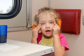 Image showing Girl makes faces four years of sitting on the train at the table on the side a place reserved seat