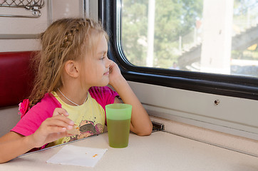 Image showing Six-year girl sitting on the train at the table on outboard second-class carriage and enthusiastically looking out the window
