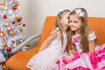 Image showing Two girls in beautiful dresses whispering sitting on couch at Christmas tree