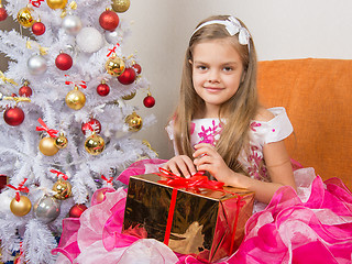 Image showing Seven-year girl in a beautiful dress sits with a gift in their hands