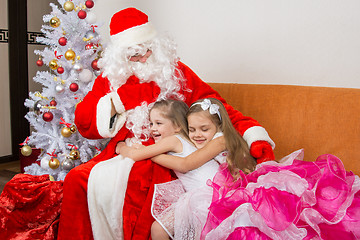 Image showing Two girls in beautiful dresses hug Santa Claus