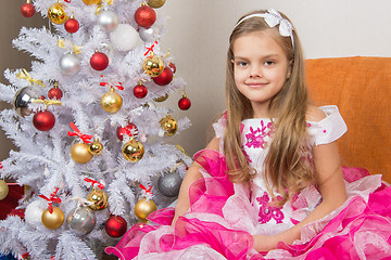 Image showing Seven-year girl sitting on a sofa in a beautiful dress the Christmas tree