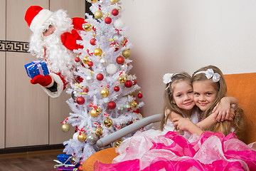 Image showing Two girls hug on the couch, santa claus peeping from behind trees