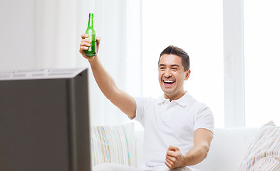 Image showing smiling man watching tv and drinking beer at home