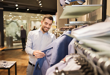 Image showing happy young man choosing clothes in clothing store