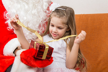 Image showing Girl unleashes a red ribbon gift in the hands of Santa Claus