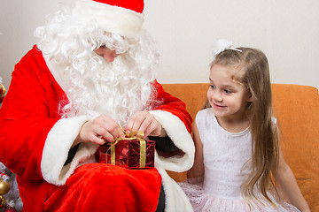 Image showing Santa Claus helps to untie the ribbon gift, little girl happily looking at him