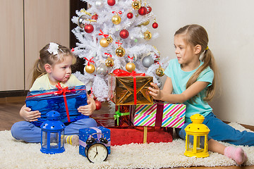 Image showing Two girls share presented New Year gifts at the Christmas tree