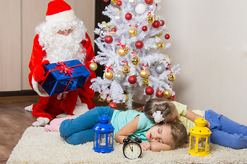 Image showing Santa Claus in New Years Eve gifts lays out and looked at the fallen asleep in front of Christmas tree two children