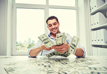 Image showing happy businessman with heap of money in office