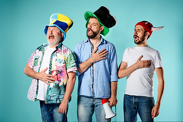 Image showing The three football fans singing the national anthem over blue