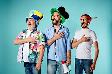 Image showing The three football fans singing the national anthem over blue