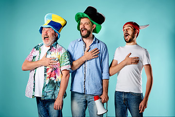 Image showing The three football fans singing the national anthem over blue