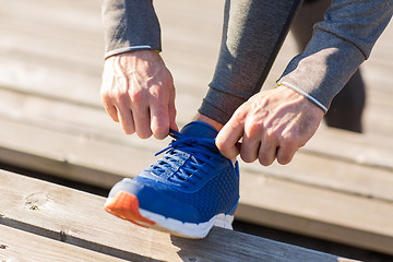 Image showing close up of sporty man tying shoe laces outdoors