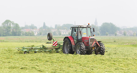 Image showing Farmer uses tractor to spread hay on the field
