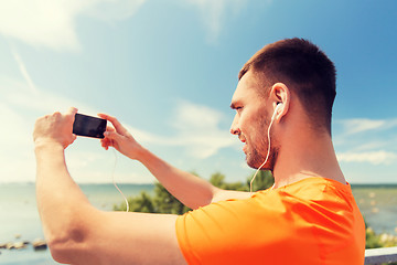 Image showing smiling young man with smartphone and earphones