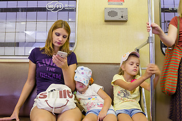 Image showing Moscow, Russia - August 10, 2015: The situation in the train of the Moscow Metro, the mother looks at the phone, the youngest daughter is asleep, the eldest of boredom clinging to the railing