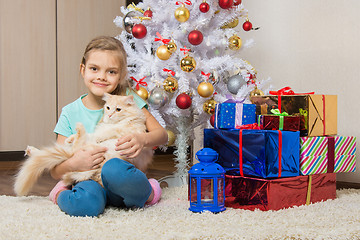 Image showing Joyful seven year old girl with a cat sitting under the Christmas tree with gifts