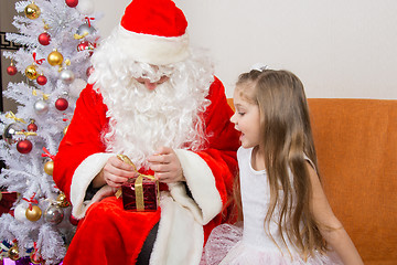 Image showing The girl with interest looks like Father Christmas helps to open her gift