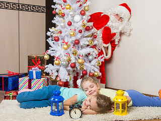 Image showing Santa Claus peeking out of a tree in front of which the two girls sleeping mat