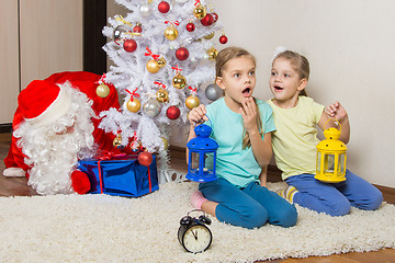 Image showing Two girls with flashlights dreaming of gifts on New Years night, and Santa Claus put presents under the Christmas tree