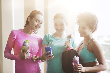 Image showing happy women with bottles and smartphone in gym