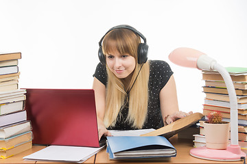 Image showing Happy student with headphones sitting at the table and looking for the information you need in a laptop