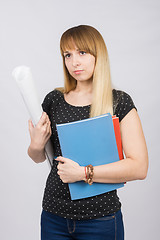 Image showing Young girl with folders and a roll of paper in the hands of a sad looking forward