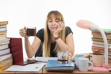 Image showing Girl student sadly and sleepily reading his thesis project sitting with a cup of coffee in hand