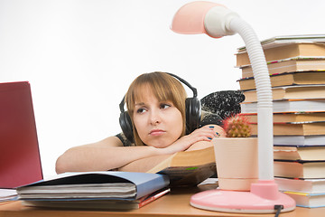 Image showing Girl sad student sitting at the table wearing headphones and listening to music