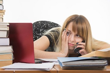 Image showing Tired young woman office worker talking on the phone and looking at monitor