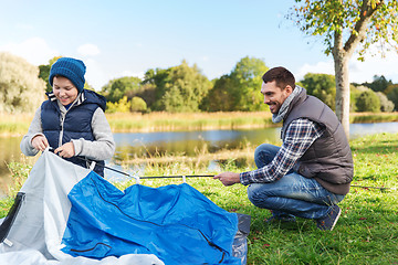 Image showing happy father and son setting up tent outdoors