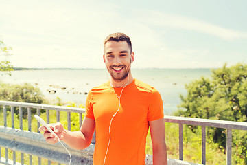 Image showing smiling young man with smartphone and earphones