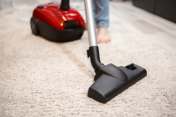 Image showing Maid cleaning carpet with modern red vacuum cleaner