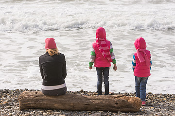 Image showing Two girls and a girl on the beach sitting on a log and looking into the distance