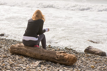 Image showing Girl sitting on the log on the coast and looks at sea