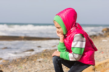 Image showing Girl sitting on the rocky beach and the sea head on his hand looking to the frame