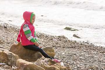 Image showing Happy girl sitting on a rock on the sea coast and looking into the distance