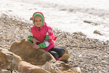 Image showing Happy girl sitting on a rock on the sea coast and looking at the frame