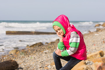 Image showing Girl sitting on the rocky beach and the sea happily lost in thought looking down