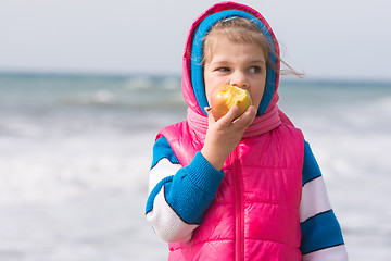 Image showing Five-year girl eating an apple on the background of the sea coast