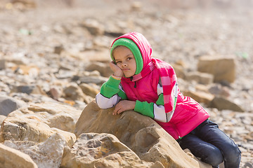 Image showing Girl bored at the seaside in the offseason lay down on a big rock