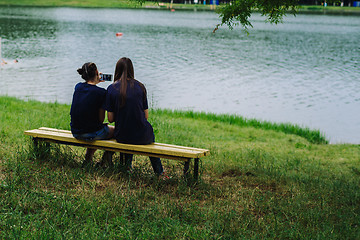 Image showing Women sit on a bench and take selfies