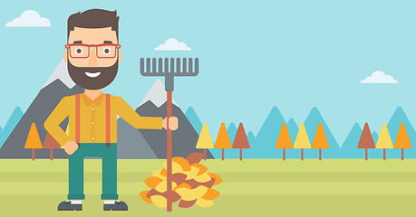Image showing Man with rake standing near heap of autumn leaves.