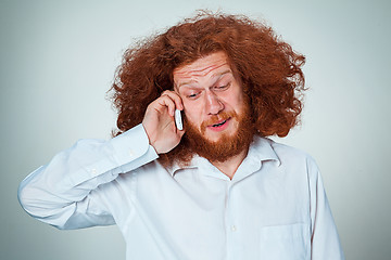 Image showing Portrait of puzzled man talking on the phone  a gray background