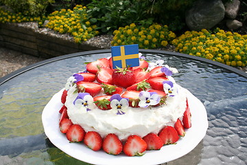 Image showing Midsummer gateau with strawberries, cream, Swedish flag  and pansies