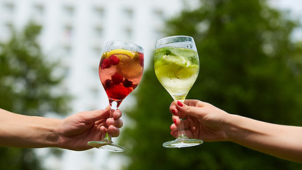 Image showing Hand holding glasses cocktail clinking together at outdoor.